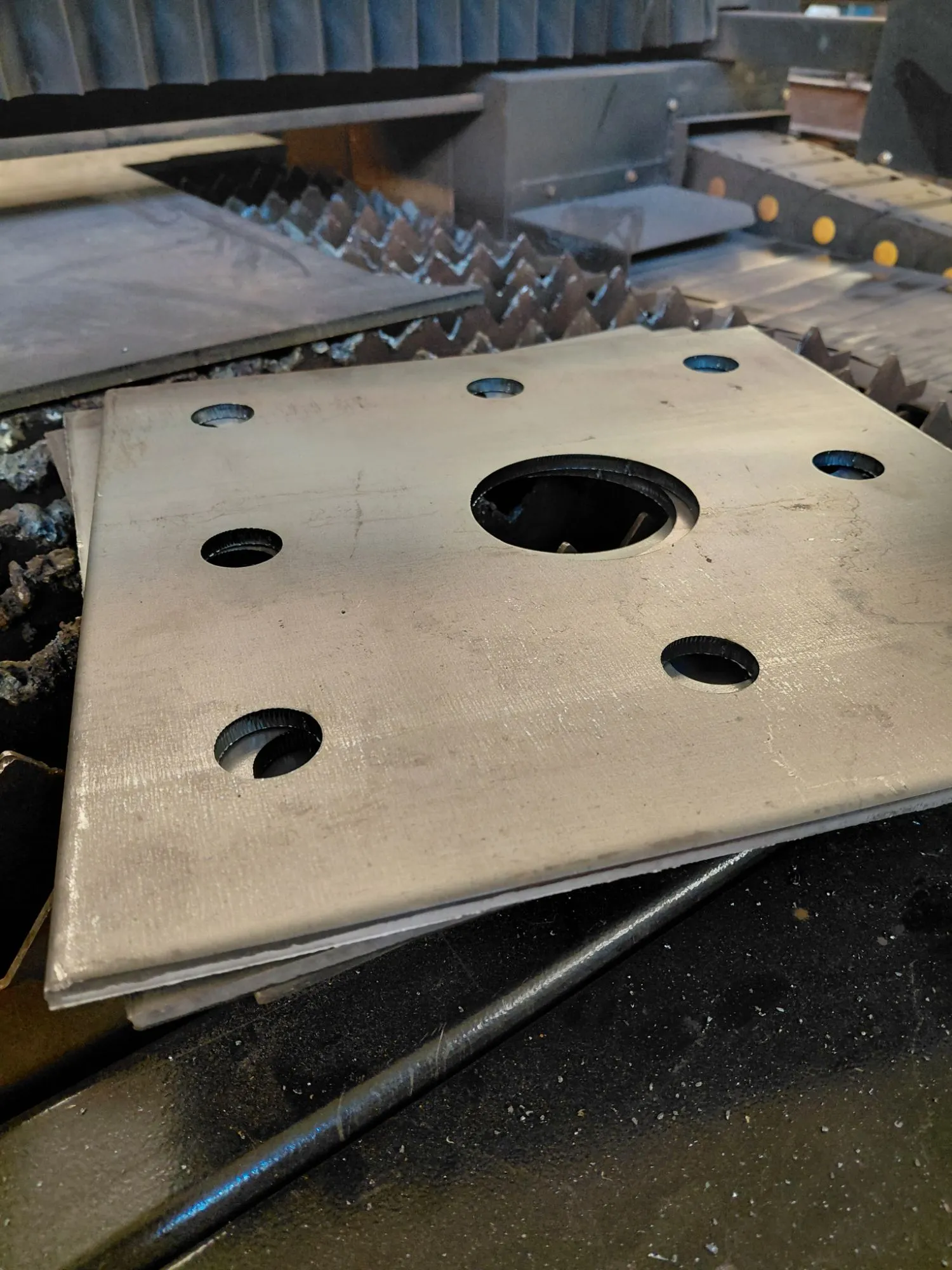 Detalle de una placa metálica cortada con láser, con perforación central y agujeros en los bordes